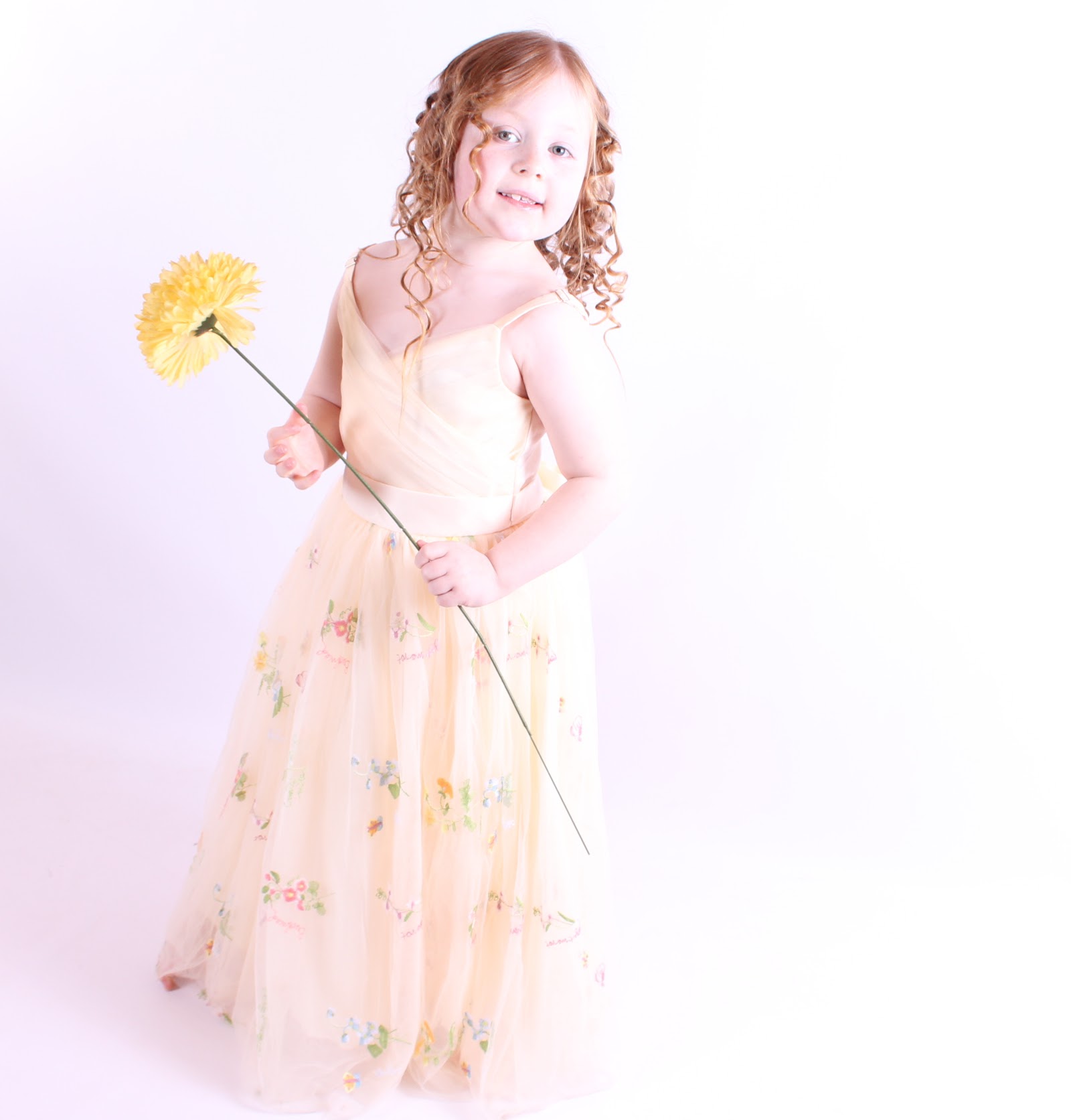 A young girl in a cream dress holding a flower in the studio